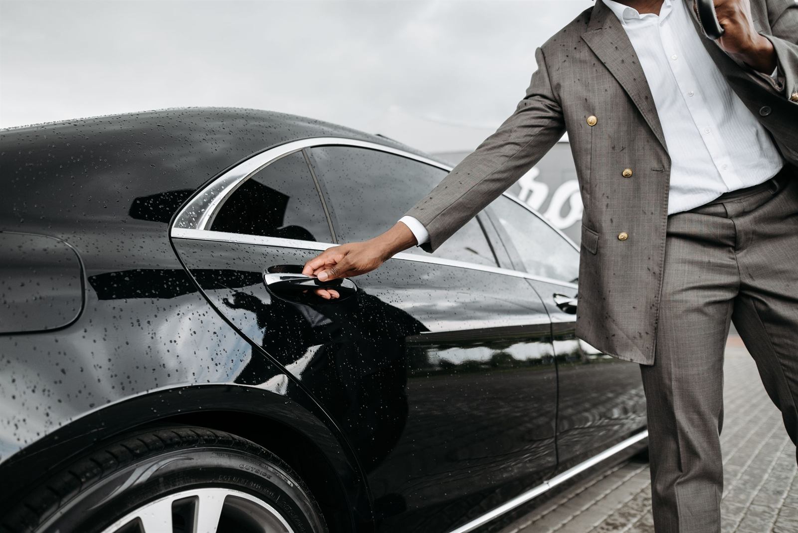 The driver's hand opening the door of a black sedan, in the rain